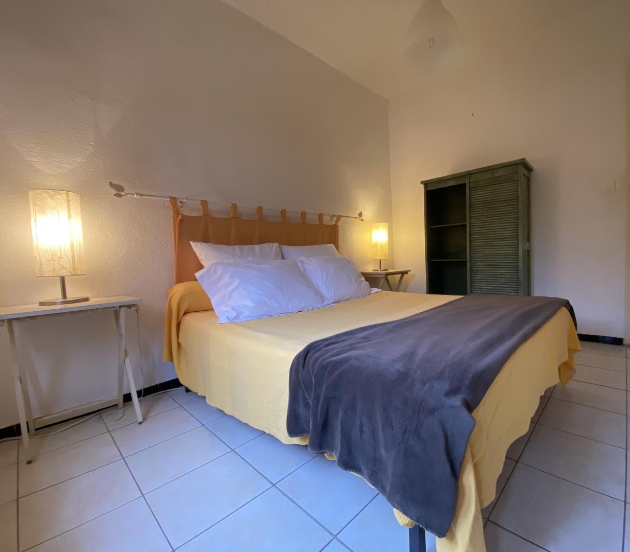 A bedroom with a bed, two bedside tables with lamps, a wardrobe, and a door.