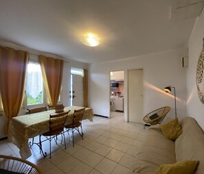 A compact living space with a dining area, a sofa, and a kitchen in the background.