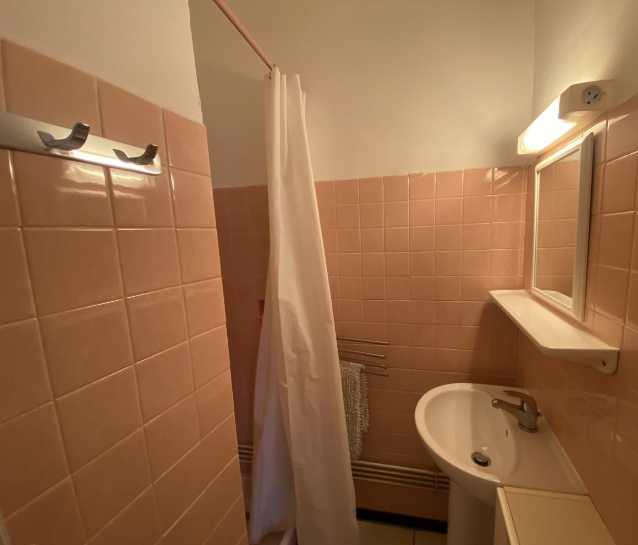 Une salle de bain avec des carreaux roses, un lavabo blanc, un miroir et un rideau de douche.