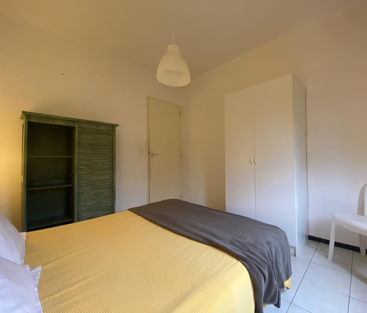 A bedroom with a bed, a wardrobe, a chair, and a hanging light fixture.