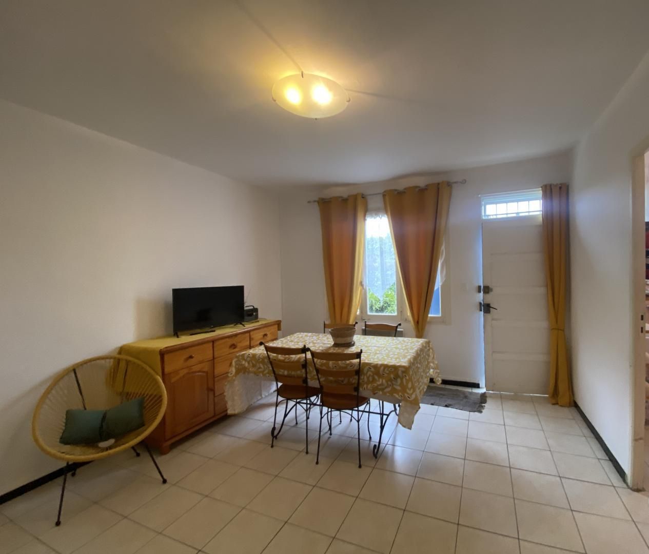 Une petite pièce propre, comprenant une table à manger, des chaises, un téléviseur et un fauteuil avec un coussin.