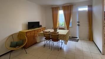 Une petite pièce propre, comprenant une table à manger, des chaises, un téléviseur et un fauteuil avec un coussin.