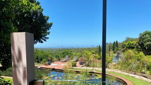 Ein Garten mit Teich, Sitzgelegenheit und Blick auf eine Stadtsilhouette.