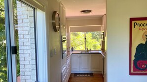 Eine Küche mit weißen Schränken, einem Edelstahlkühlschrank und einem Fenster mit Blick auf Bäume.