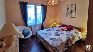 A bedroom with a bed, a chair, a window with curtains, a hanging light fixture, and a wall art piece. - Pause Colliourencque (COLLIOURE)