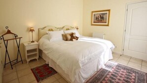 Une chambre à coucher bien rangée, avec un lit, des tables de chevet, un radiateur, une porte et un tableau encadré au mur.