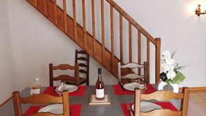 A dining area with a wooden staircase, wooden chairs, a table set with red placemats, wine glasses, and a bottle of wine.
