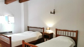Two wooden beds with white linens in a room with white walls and a tiled floor.