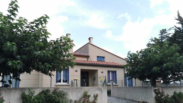 A two-story house with a tiled roof, a visible door, and a small balcony.