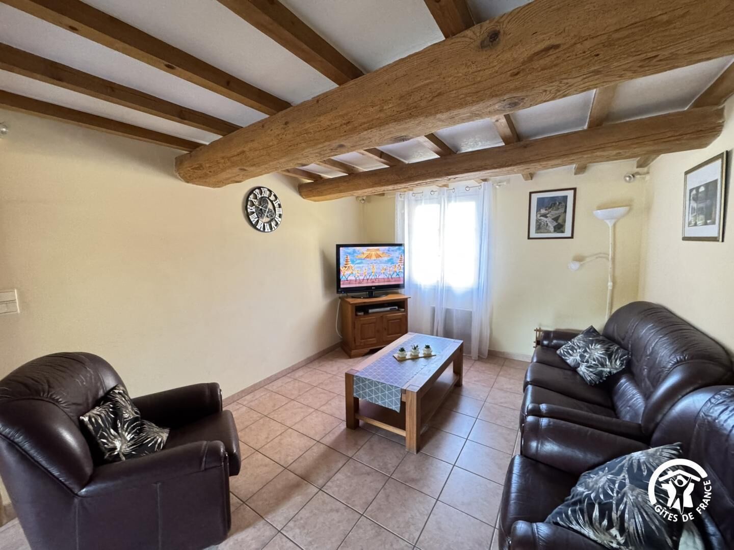 A living room with a wooden ceiling, a television, two leather sofas, a coffee table, and a clock on the wall.