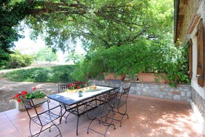 An outdoor patio with a table and chairs, surrounded by greenery and stone walls. - La marinade - ELNE - Gîte (ELNE)