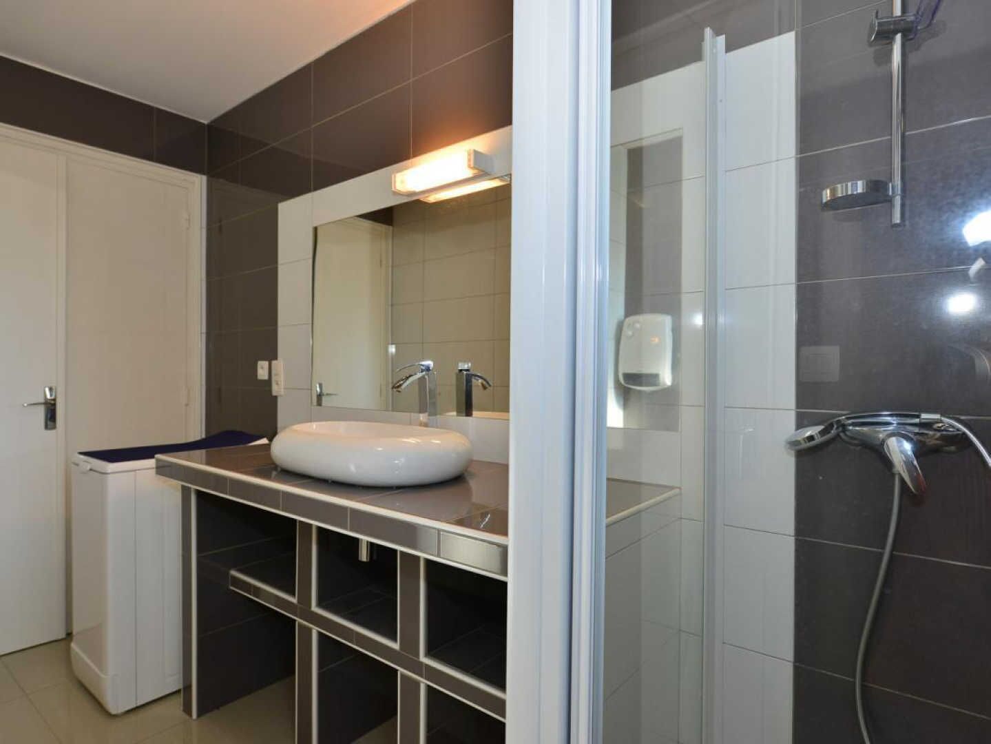 A modern bathroom with a white sink, a large mirror, and a glass-enclosed shower area.