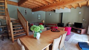Een houten eettafel met rieten stoelen, een trap, een bank, een televisie en een open haard.