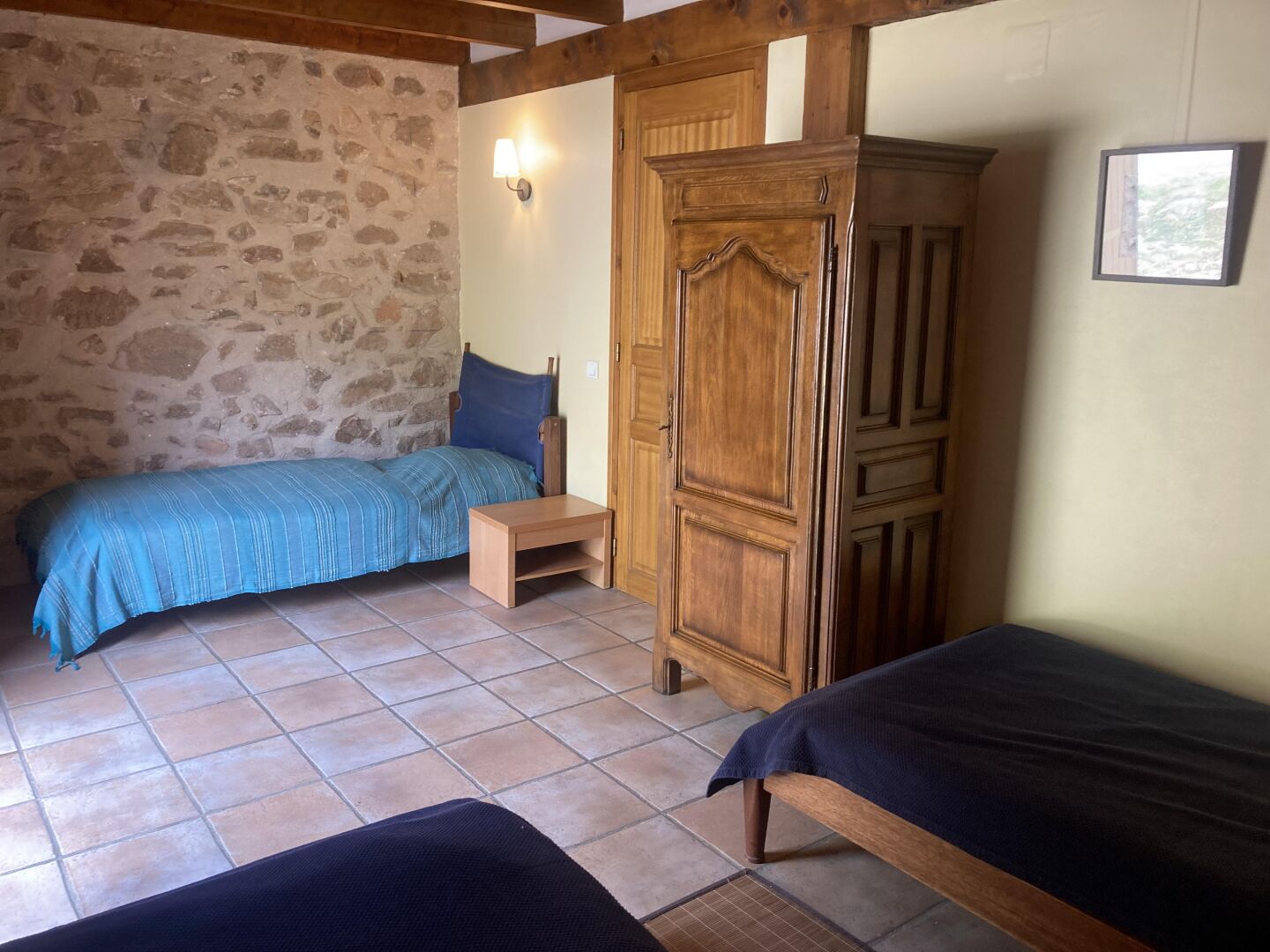 A room with two beds, a wooden wardrobe, a stone wall, and a tiled floor.