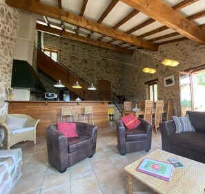 Un intérieur rustique avec des murs en pierre, des poutres en bois, un coin cuisine et des espaces aménagés pour s’asseoir.