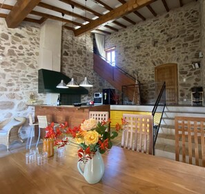 Une cuisine rustique aux murs de pierre, avec des poutres en bois et un coin repas comprenant une table et des chaises en bois.