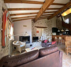 Un intérieur rustique avec des poutres apparentes, un mur en pierre, une cheminée, un canapé, un téléviseur et un coin bar.