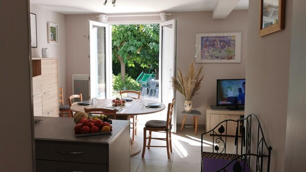 A dining area with a table set for two, chairs, a cabinet with drawers, a television on a stand, and a window with a view of greenery outside. - L'arbousier - SAINT CYPRIEN (SAINT CYPRIEN)