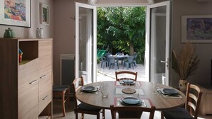 A dining area with a round table set for four, a wooden cabinet, and a view of an outdoor patio with chairs and greenery. - L'arbousier - SAINT CYPRIEN (SAINT CYPRIEN)