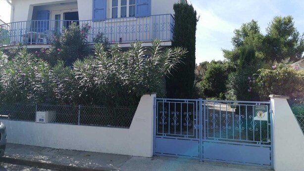Una casa de dos pisos con un balcón, una reja metálica y diversas plantas.