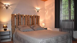 Un dormitorio con cabecera de madera, dos lámparas de noche, una cama con ropa de cama estampada y una ventana con cortinas.