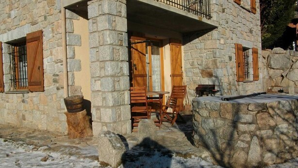 Un edificio de piedra con un balcón, contraventanas de madera y un espacio al aire libre rústico con mobiliario.