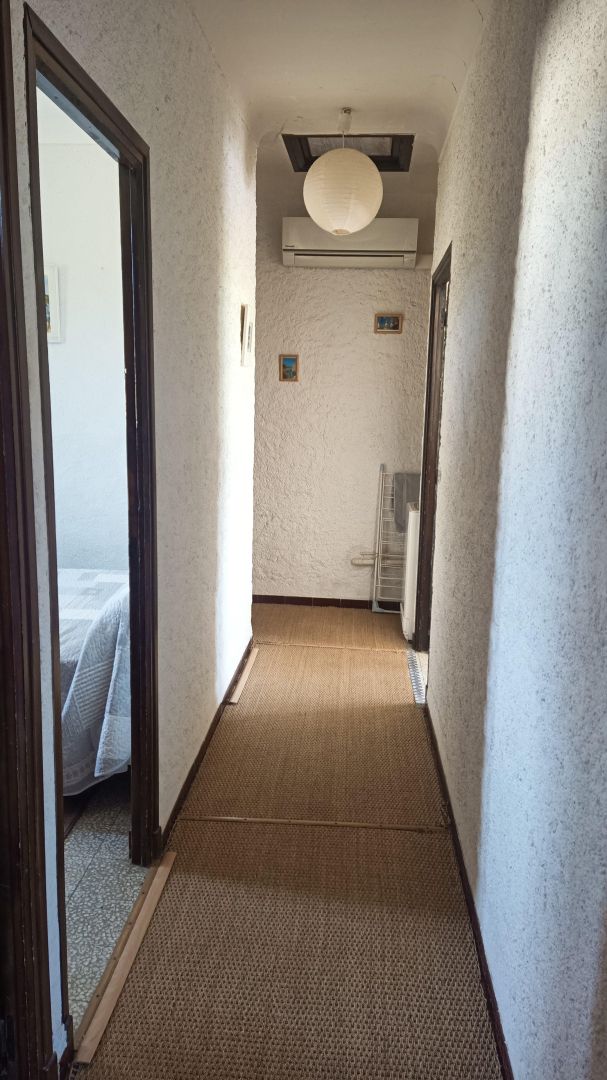 A narrow hallway with a textured floor, a ceiling fan, and a wall-mounted air conditioner.