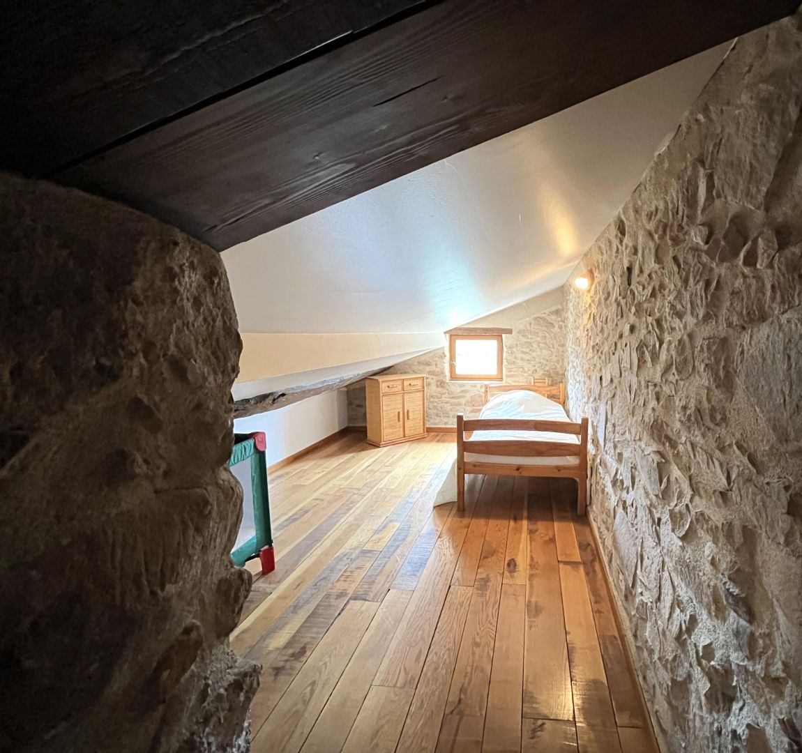 Een rustieke slaapkamer op zolder met een houten bed, stenen muren en een schuine plafond.