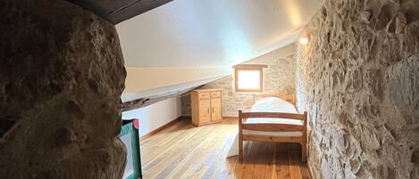 A rustic attic bedroom with a wooden bed, stone walls, and a sloped ceiling.