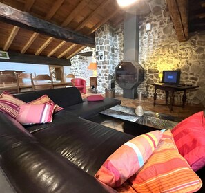 A cozy living room with a stone wall, a fireplace, a black leather sofa, and a television. - Cal cabre - ST LAURENT DE CERDANS (ST LAURENT DE CERDANS)