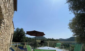 A terrace with a table, chairs, and an umbrella, overlooking a mountainous landscape.