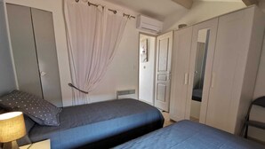 A bedroom with two beds, a nightstand, a lamp, a wardrobe, and a door.