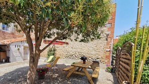 A patio with a wooden table and chairs, surrounded by gravel and a tree.