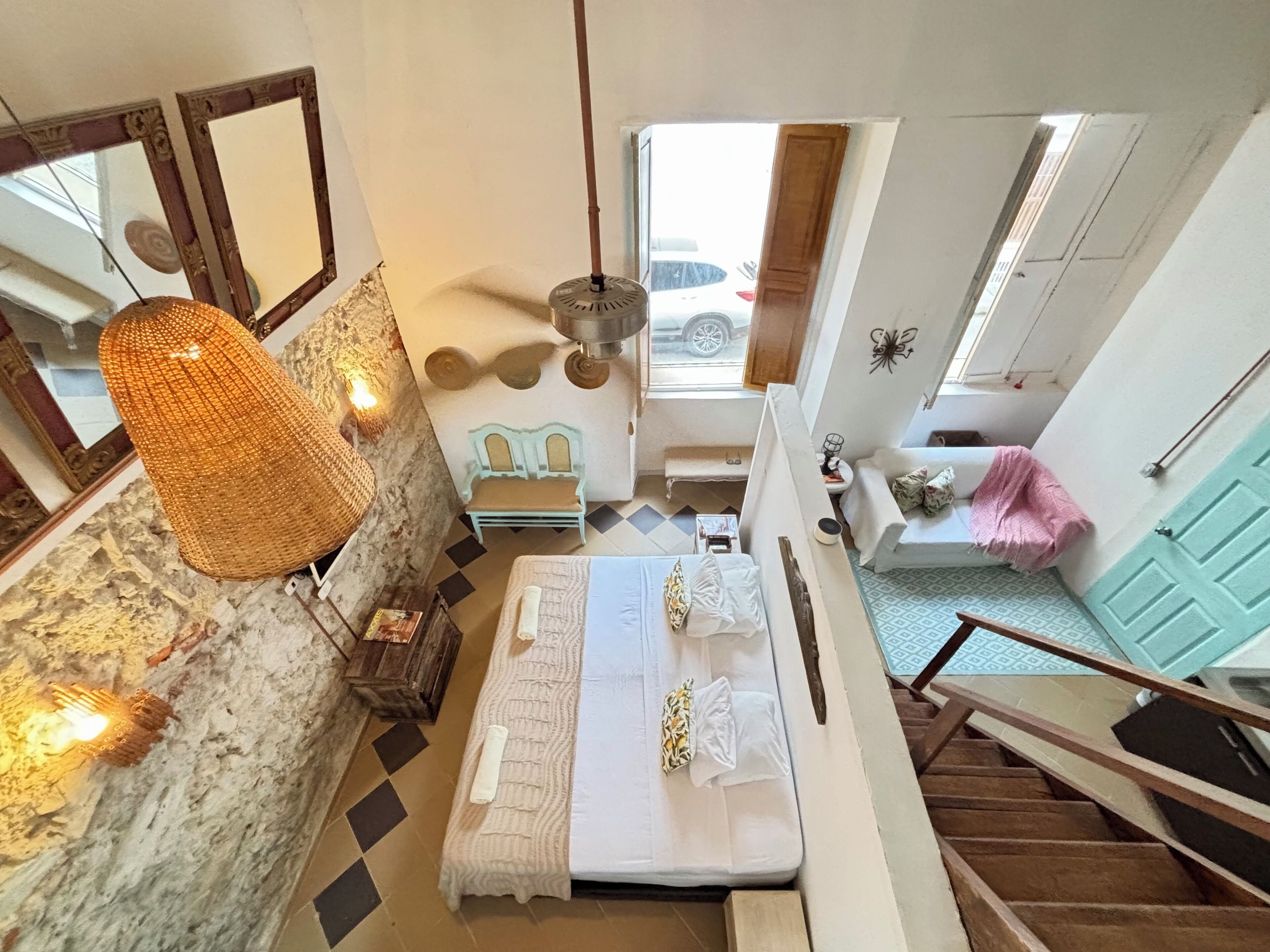 Une chambre à coucher avec un lit, une petite table, un banc, une lampe suspendue et une vue sur l’extérieur.