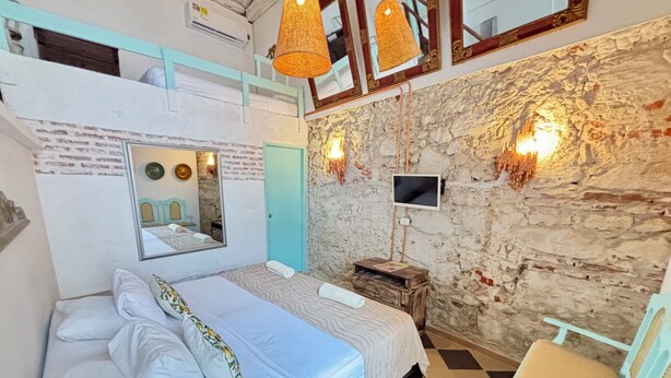 A bedroom with a bed, a chair, a TV, and a mirror. - Colonial Loft Studio in the best location in the walled city of Ctg. (Cartagena de Indias)