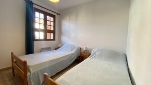 Ett litet, rent rum med två enkelsängar, ett fönster med gardiner, en värmare och en sänglampa.