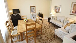 A living room with a wooden dining table, chairs, a sofa, and a television.