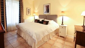 A hotel room with a large bed, two bedside tables with lamps, a radiator, and a window with curtains.