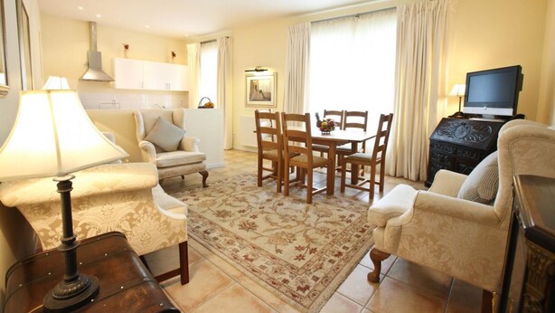 A living room with a sofa, armchair, dining table, chairs, a TV, and a lamp.