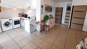 Une cuisine compacte équipée d’un lave-linge, d’un four, d’un four à micro-ondes et d’un petit coin repas avec une chaise et une table.