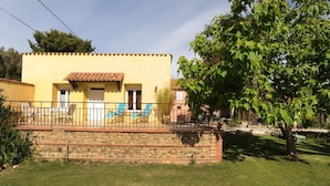 Un bâtiment jaune avec un toit en tuiles, un mur en pierre et une terrasse clôturée aménagée avec des chaises longues.