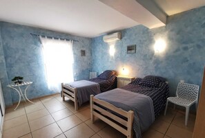 A bedroom with two wooden beds, a small table with a plant, a chair, and an air conditioning unit on the wall. - Domitia - PERPIGNAN - Gîte (PERPIGNAN)