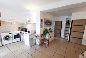 A compact kitchen with a washing machine, oven, microwave, and a small dining area with a chair and table. - Domitia - PERPIGNAN - Gîte (PERPIGNAN)