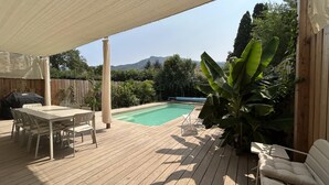 En træterrasse med pool, udendørs møbler og udsigt til bjerge.