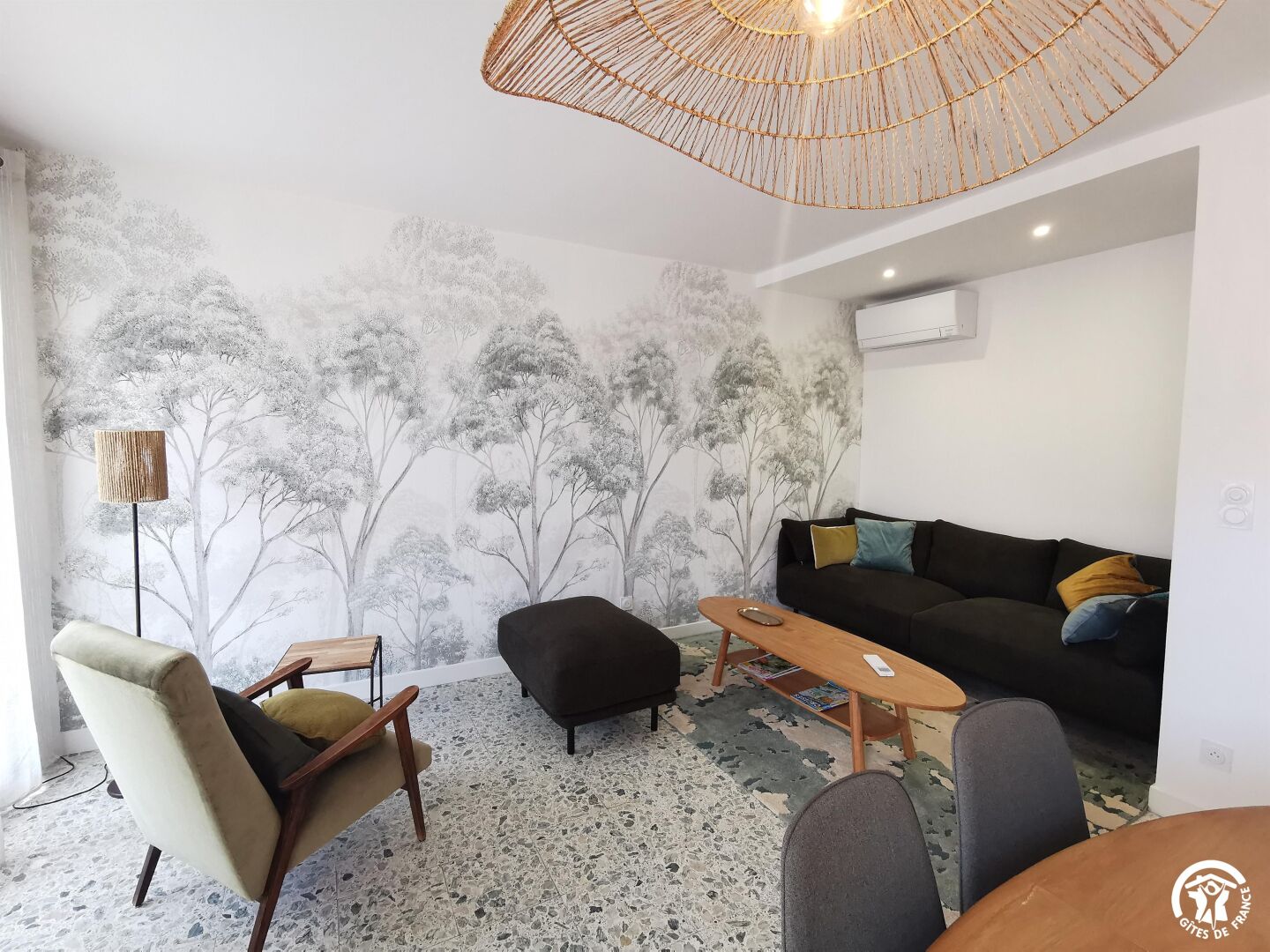 Una sala de estar moderna con un sofá, sillones, una mesa de centro y un mural en la pared con motivos de árboles.