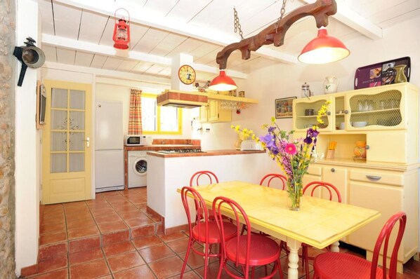 A compact kitchen with a dining area, a washing machine, a stove, and a clock on the wall.