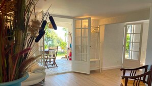 A spacious room with a wooden floor, a white sofa, a wooden chair, and a large window. - Les micoucouliers - LAROQUE-DES-ALBERES (LAROQUE-DES-ALBERES)