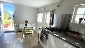 A modern kitchen with a gas stove, oven, and stainless steel appliances. There is a dining area with a table and chairs, and a view of the outdoors through a sliding door. - Les micoucouliers - LAROQUE-DES-ALBERES (LAROQUE-DES-ALBERES)