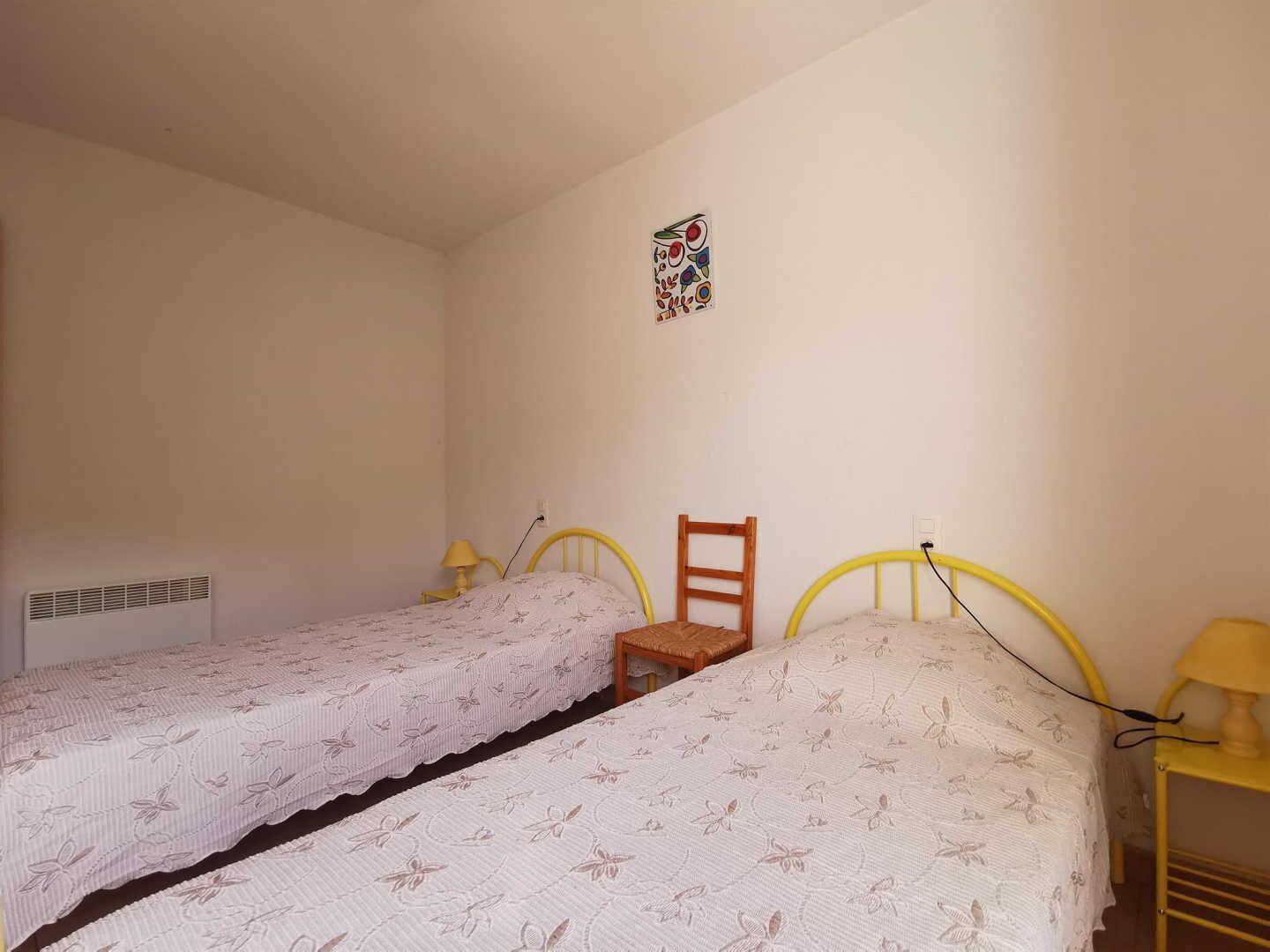 Un dormitorio con dos camas individuales, una silla, una decoraci ón en la pared y un radiador.