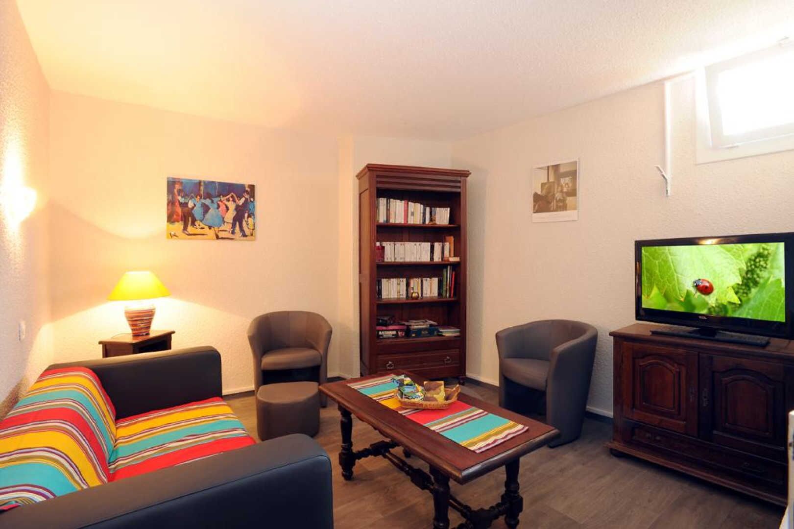 A living room with a sofa, two armchairs, a coffee table, a bookshelf, a television, and a lamp.